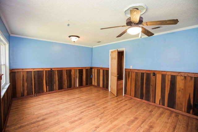unfurnished room featuring a wainscoted wall, a textured ceiling, crown molding, ceiling fan, and wood finished floors