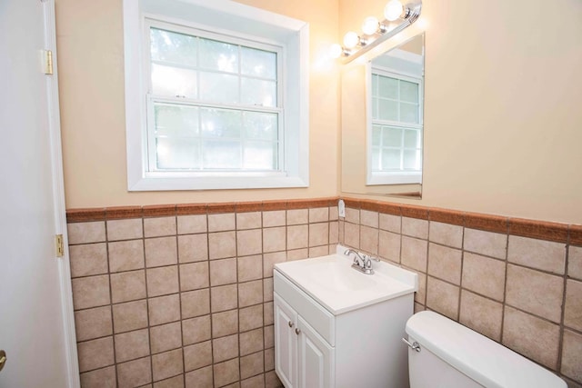 half bathroom with toilet, vanity, a wainscoted wall, and tile walls