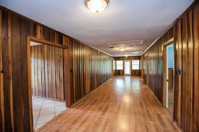 corridor with wood walls, crown molding, attic access, and a textured ceiling