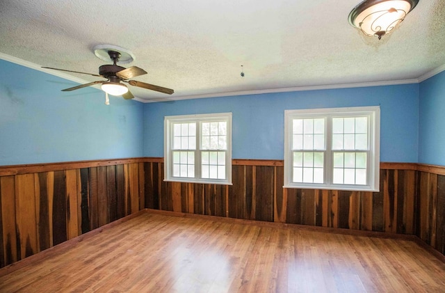 empty room featuring a wainscoted wall, wood finished floors, wood walls, and a textured ceiling