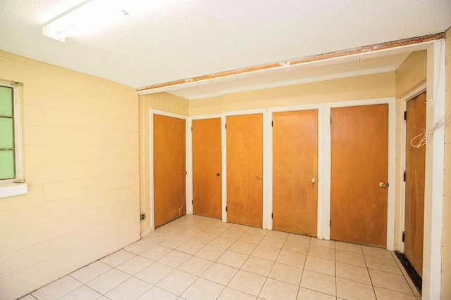 unfurnished bedroom with a textured ceiling, concrete block wall, and two closets