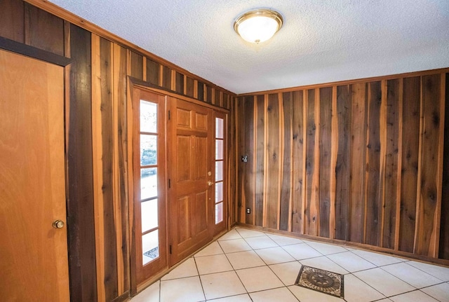 foyer featuring light tile patterned floors, wooden walls, and a textured ceiling
