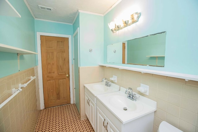 bathroom with tile walls, visible vents, a sink, and wainscoting