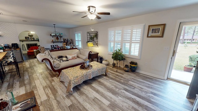 living room featuring ceiling fan, a fireplace, visible vents, baseboards, and light wood-type flooring