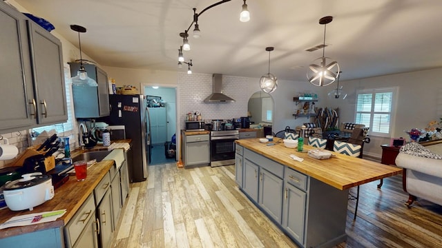 kitchen featuring visible vents, hanging light fixtures, appliances with stainless steel finishes, wood counters, and wall chimney exhaust hood