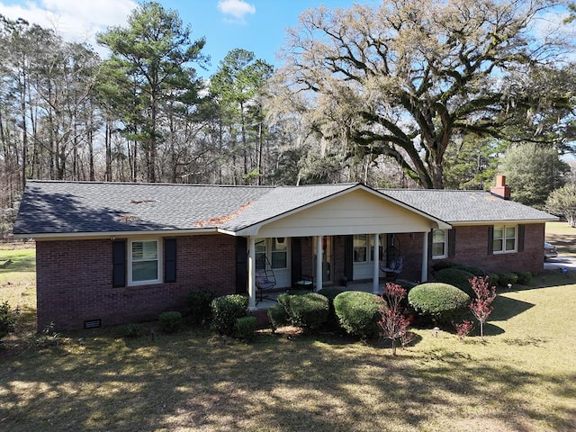 ranch-style home featuring a shingled roof, crawl space, covered porch, a front lawn, and brick siding