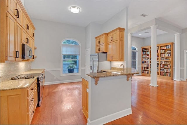 kitchen with ornate columns, appliances with stainless steel finishes, light wood finished floors, and light brown cabinets