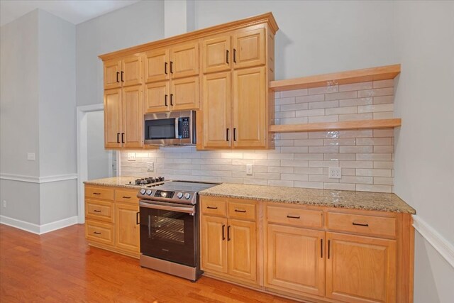 kitchen with open shelves, light stone countertops, stainless steel appliances, decorative backsplash, and light wood-type flooring