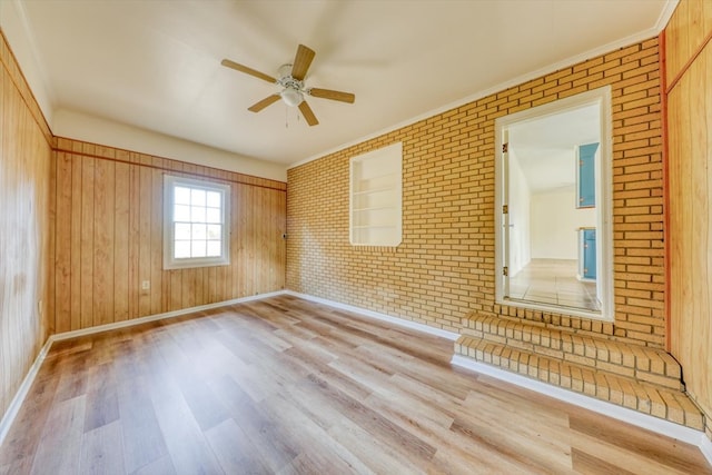 empty room featuring crown molding, brick wall, ceiling fan, and light wood-type flooring