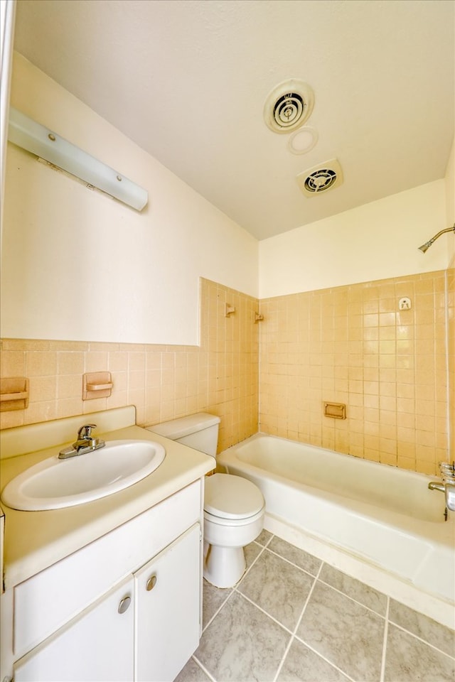 full bathroom with toilet, tiled shower / bath, tile walls, vanity, and tile patterned flooring