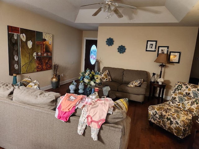 living area featuring a tray ceiling, wood finished floors, ceiling fan, and baseboards