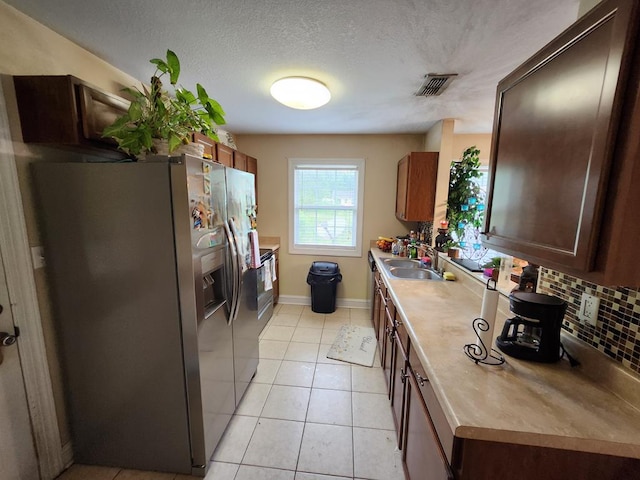 kitchen with stainless steel fridge, a sink, backsplash, light countertops, and a textured ceiling