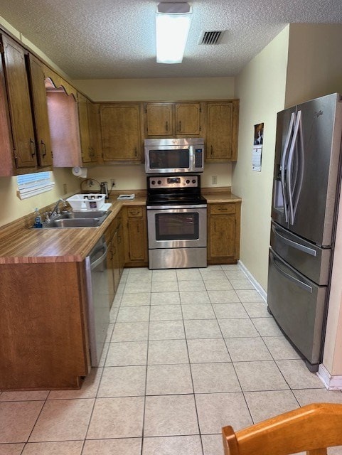 kitchen featuring appliances with stainless steel finishes, sink, light tile patterned floors, and a textured ceiling