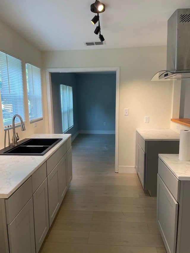 kitchen featuring baseboards, visible vents, wall chimney exhaust hood, light wood-style flooring, and a sink