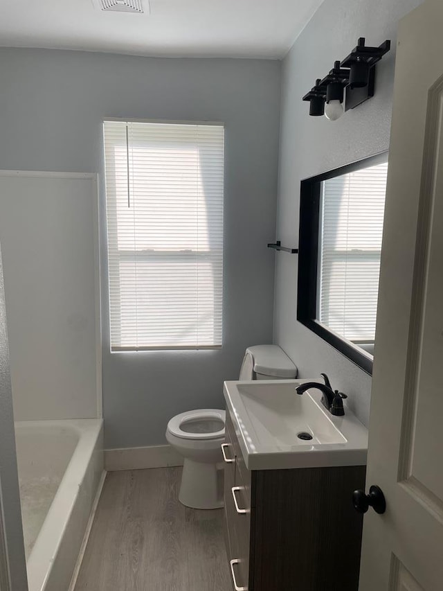 full bathroom with toilet, a bathing tub, vanity, wood finished floors, and baseboards