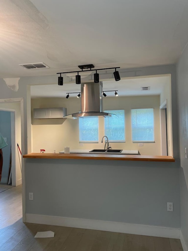 kitchen with visible vents, baseboards, wood finished floors, island exhaust hood, and a sink