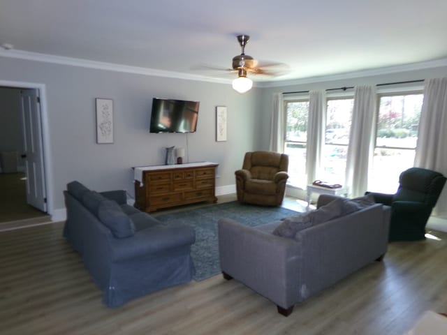 living room featuring ornamental molding, light wood-style flooring, baseboards, and a ceiling fan