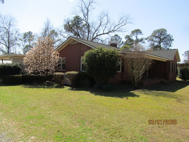 view of side of property with a chimney, a lawn, and brick siding