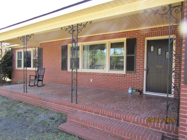 doorway to property with covered porch and brick siding