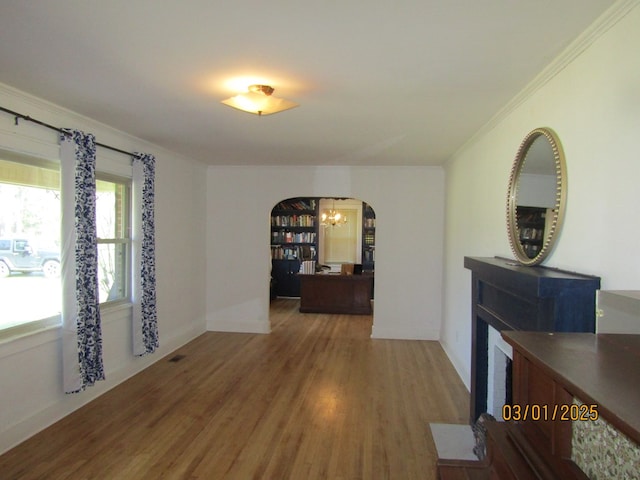 interior space featuring arched walkways, a notable chandelier, wood finished floors, baseboards, and ornamental molding