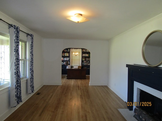 interior space featuring arched walkways, an inviting chandelier, ornamental molding, wood finished floors, and baseboards