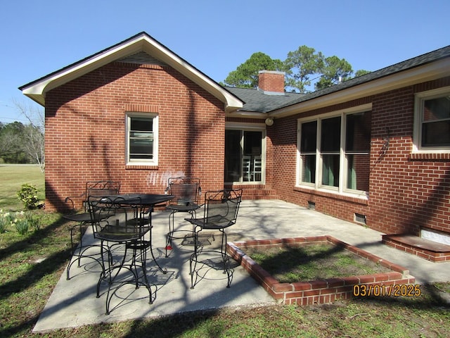 rear view of property with a chimney, a patio, and brick siding