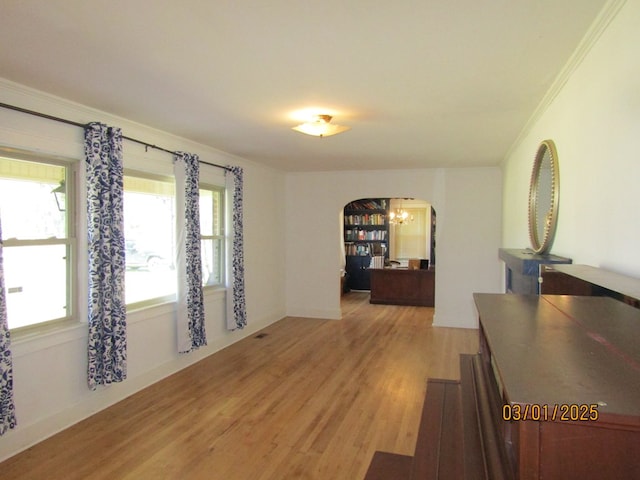 interior space with arched walkways, crown molding, and light wood finished floors