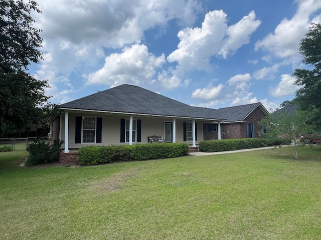 view of front of home featuring covered porch, fence, roof with shingles, and a front lawn