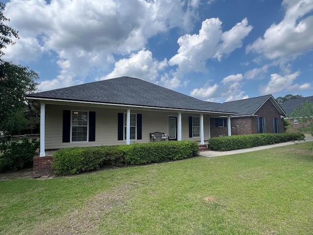 ranch-style house featuring covered porch, a shingled roof, and a front yard