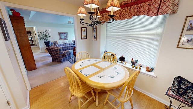 dining room with baseboards, light wood-style flooring, and ceiling fan with notable chandelier