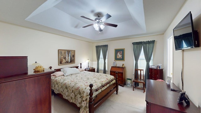 bedroom with a raised ceiling, ceiling fan, and light carpet