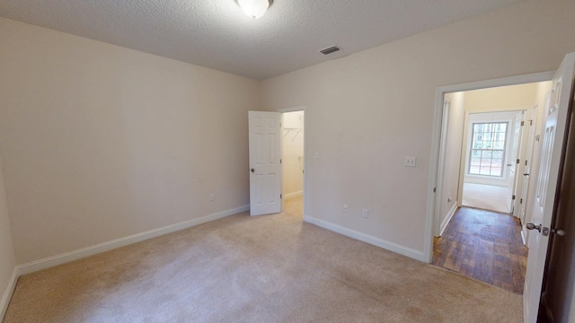 unfurnished bedroom with visible vents, a textured ceiling, carpet floors, baseboards, and a spacious closet