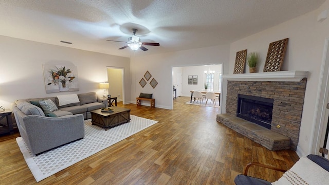 living room featuring wood finished floors, baseboards, visible vents, a textured ceiling, and ceiling fan with notable chandelier