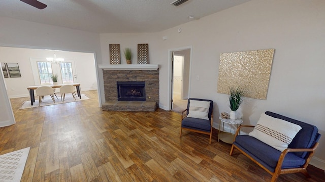 living area featuring a notable chandelier, a textured ceiling, wood finished floors, a stone fireplace, and baseboards