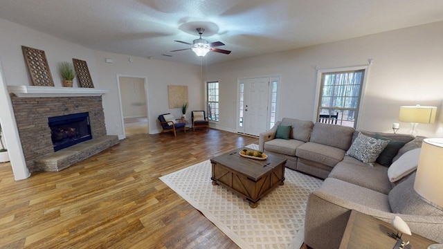 living area featuring a stone fireplace, a ceiling fan, light wood-type flooring, and baseboards