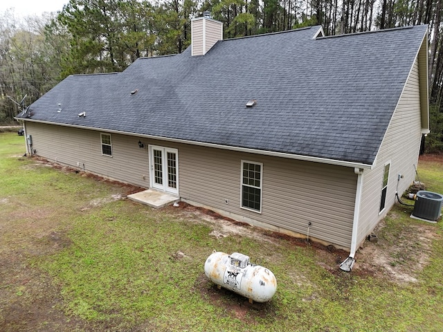 rear view of house with central air condition unit, roof with shingles, french doors, a chimney, and a yard