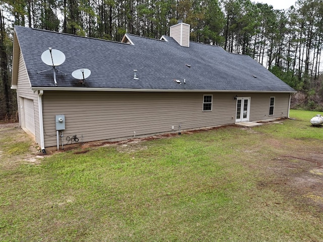 back of house with a shingled roof, french doors, a chimney, a garage, and a yard