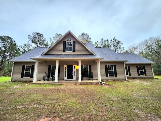 view of front of house featuring a shingled roof, a porch, a yard, and a chimney