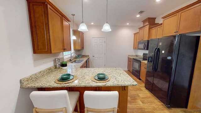 kitchen with black appliances, a sink, light stone counters, a peninsula, and light wood finished floors