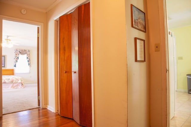 corridor with light wood-style flooring, crown molding, and baseboards
