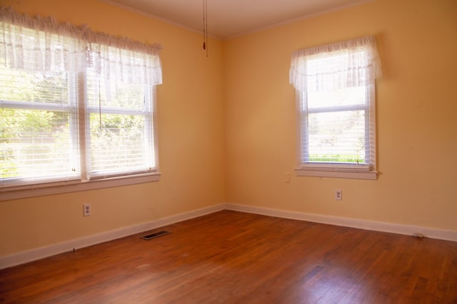 spare room featuring crown molding, visible vents, baseboards, and wood finished floors