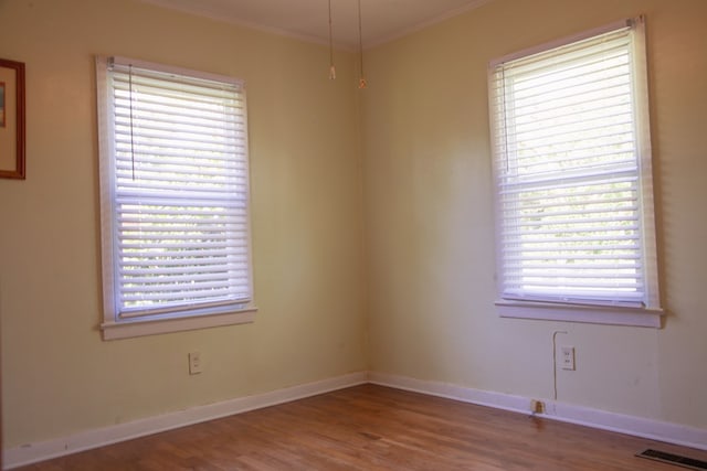 unfurnished room featuring crown molding, visible vents, baseboards, and wood finished floors