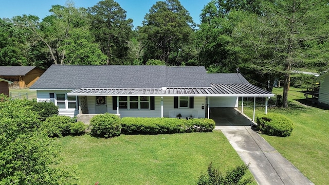 view of front facade with a front yard, a shingled roof, an attached carport, and driveway