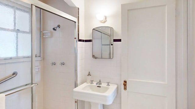 bathroom with a shower with door, sink, and tile walls