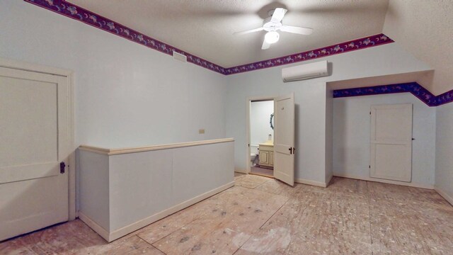 unfurnished bedroom featuring ceiling fan, ensuite bathroom, a wall mounted AC, and a textured ceiling