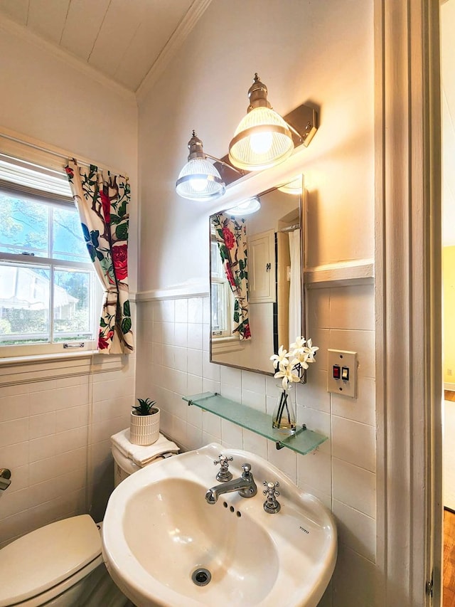 bathroom with crown molding, toilet, sink, and tile walls