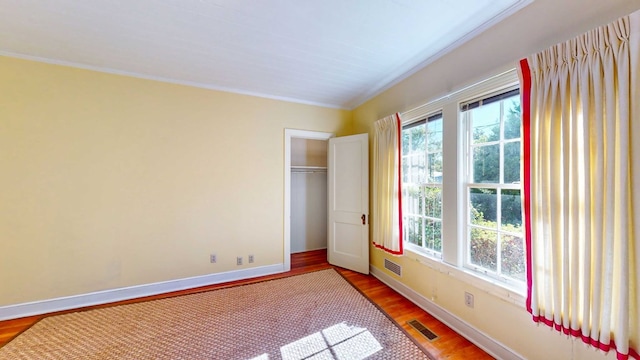 unfurnished bedroom featuring a closet, ornamental molding, hardwood / wood-style floors, and multiple windows