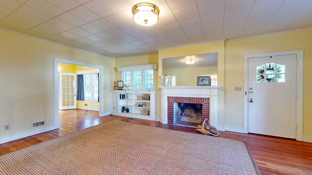 unfurnished living room with ornamental molding, a brick fireplace, and wood-type flooring