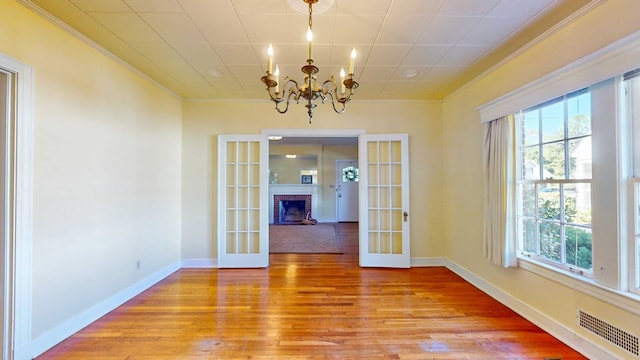 unfurnished dining area featuring a fireplace, a chandelier, crown molding, light wood-type flooring, and french doors