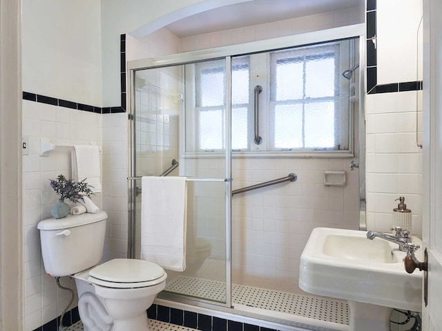 bathroom featuring tile walls, sink, a shower with door, and toilet